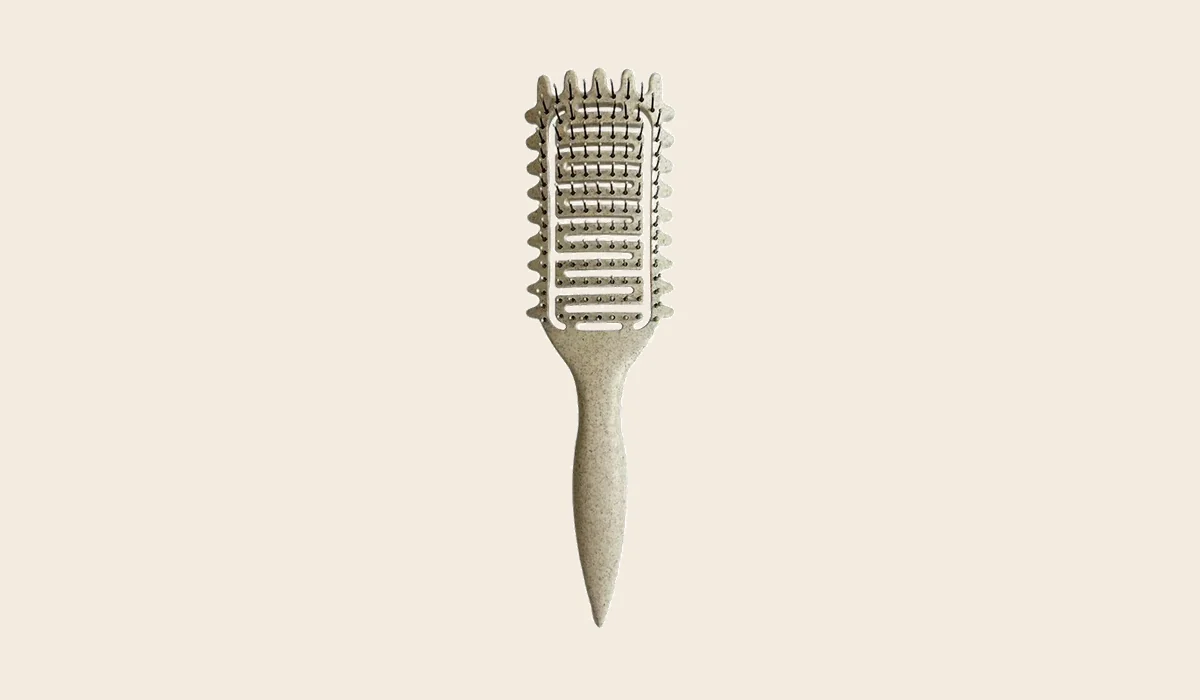 Une brosse à boucles ajourée posée à sécher picots vers le bas sur une serviette pliée, au bord d'un lavabo